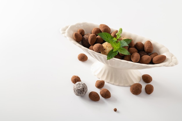Natuurlijke chocoladetruffels met munt in decoratieve schotels, witte achtergrond