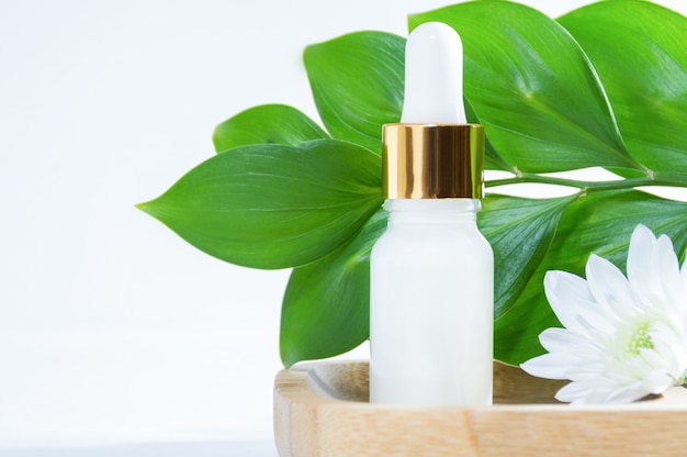 Natuurlijke cosmetica: serum met druppelaar, witte bloem en groene bladeren