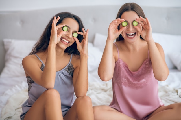 Natuurlijke cosmetica. Twee schattige jonge meisjes met plakjes komkommer in handen