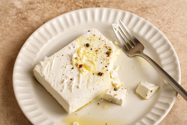 Natuurlijke gemarineerde Griekse fetakaas op wit bord met olijfolie en kruidenpeper Vork beige tafel