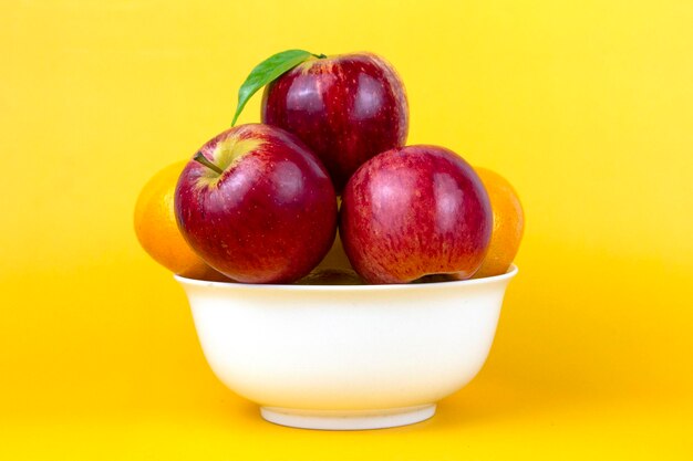 Natuurlijke gezonde vruchten in een witte kom groene appels rode appels sinaasappels geïsoleerd op gele achtergrond Creatieve samenstelling van kleurrijke vruchten geïsoleerd op gele achtergrond