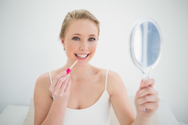 Natuurlijke glimlachende blonde holdingsspiegel en het toepassen van lipgloss