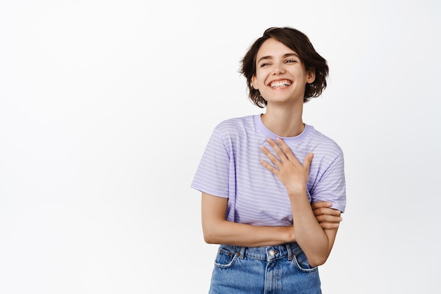 Natuurlijke jonge vrouw lachen en glimlachen, staande in tshirt en jeans tegen een witte achtergrond.