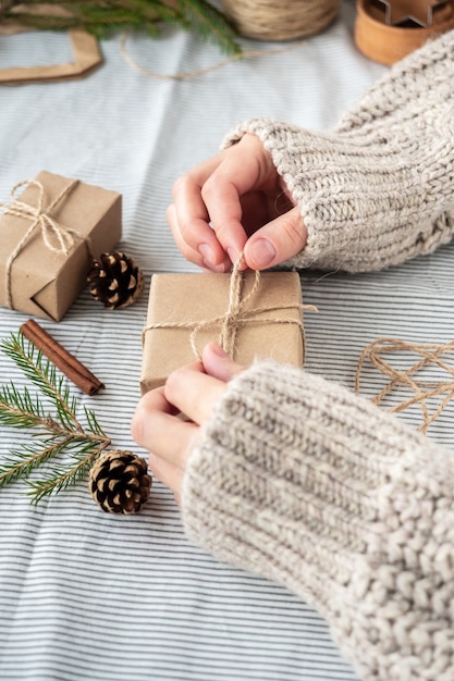 Foto natuurlijke kerstachtergrond, ambachtelijke geschenkdozen, kegels, kerstboom op tafel, close-up, retro-stijl. een meisje in een trui is cadeautjes aan het inpakken. de vrolijke sfeer van de vakantie.
