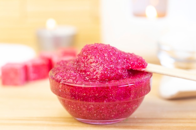 Natuurlijke roze bodyscrub gemaakt van suiker. Roze schrob in een glaskop op een achtergrond van kaarsen en suiker.