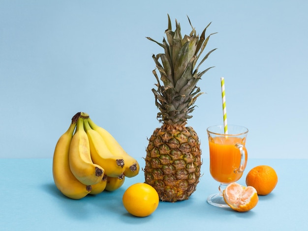 Natuurlijke samenstelling van tropisch fruit. Bananen, verse ananas, mandarijn en citroen met glas vruchtensap op blauwe achtergrond.