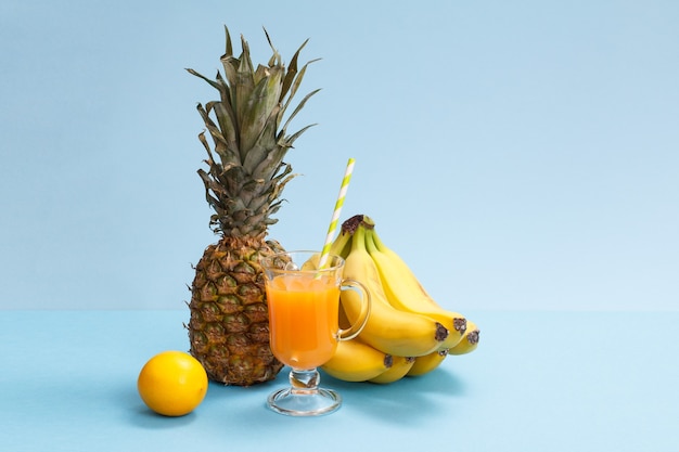 Natuurlijke samenstelling van tropisch fruit. Verse ananas, bananen en citroen met glas vruchtensap op blauwe achtergrond.