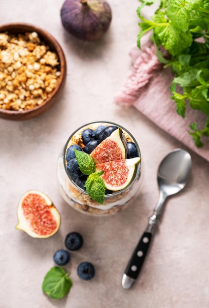 Natuurlijke yoghurt met muesli vijgen en bessen in een glas op een roze achtergrond met munt