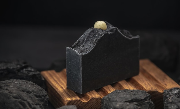 Natuurlijke zwarte houtskoolzeep in een houten zeepbakje omringd door kolen Concept van het maken en gebruiken van biologische zeep en cosmetica eco handgemaakte cadeaus
