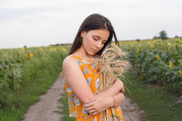 Natuurportret Close-up van mooie vrouw in jurk houdt tarweoogst in haar handen terwijl ze in een geel tarweveld staat