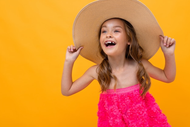 Naughty cheerful girl in a pink dress and a straw hat on a background of a yellow wall