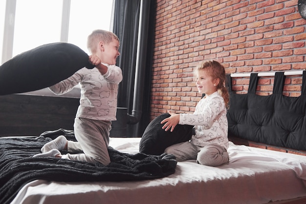 Bambini cattivi ragazzino e ragazza hanno organizzato una lotta con i cuscini sul letto in camera da letto. a loro piace quel tipo di gioco