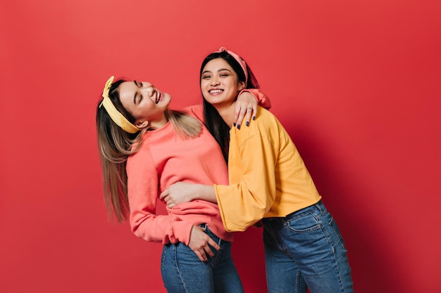 Naughty women in headbands and sweatshirts laugh on red background