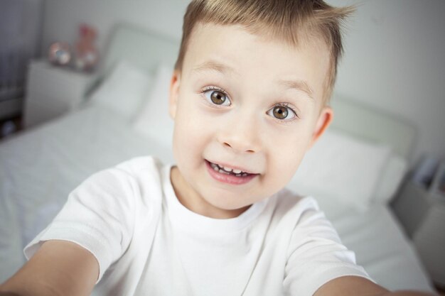 Nauw portret van een schattige kleine blonde jongen van 4 jaar oud Het kind trekt een grimas naar de camera Gelukkig kind Gezellig thuis