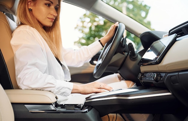 Навигация по интерфейсу автомобиля Молодая женщина в белой одежде со своим электромобилем днем