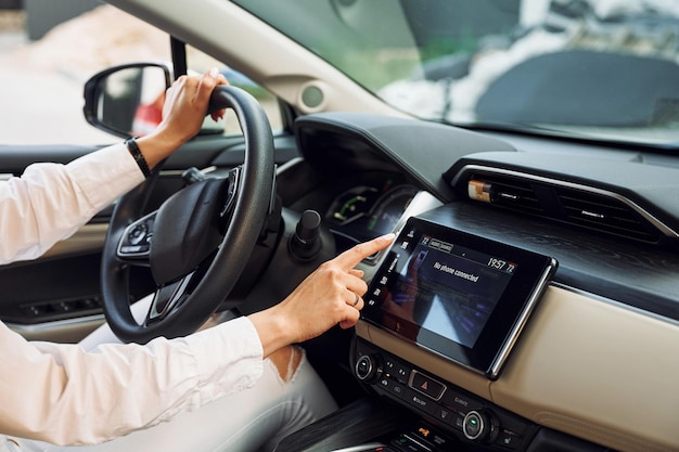 Navigeren door de interface van het voertuig jonge vrouw in witte kleren rijdt overdag met haar elektrische auto