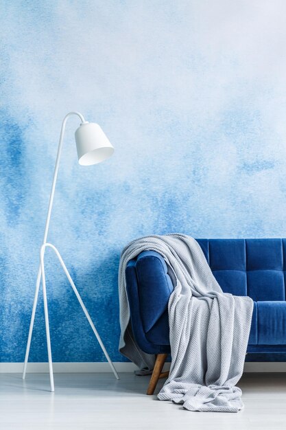 Photo navy blue couch with gray blanket and white standing lamp against blue and white ombre wall in a living room interior real photo