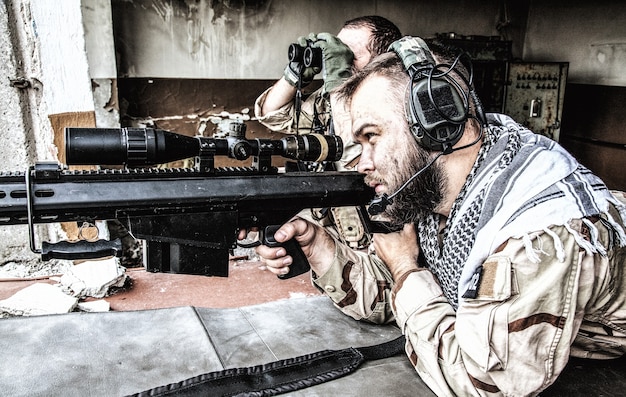 Navy SEAL sniper team, armed 50 caliber sniper rifle, observing territory, waiting in ambush, enemy forces surveillance, searching and engaging targets on range from position in city ruined building