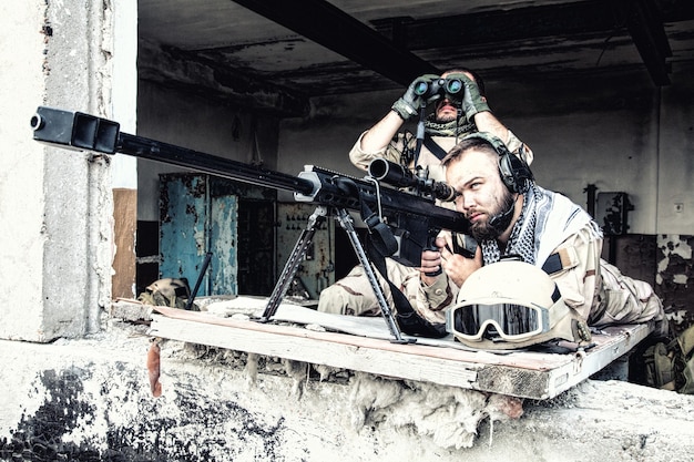 Photo navy seal sniper team, armed 50 caliber sniper rifle, observing territory, waiting in ambush, enemy forces surveillance, searching and engaging targets on range from position in city ruined building