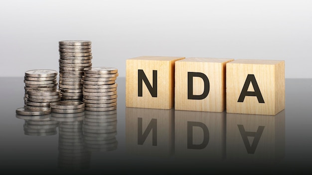 Nda text on wooden cubes on a cold grey light background with stacks coins