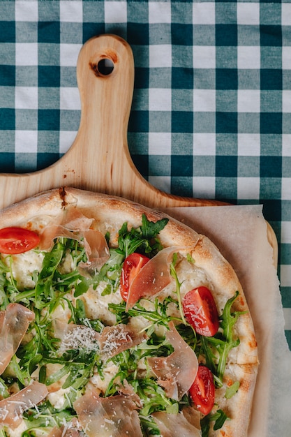 Pizza napoletana con salame, rucola, pomodori cosparsi di formaggio su una tavola di legno