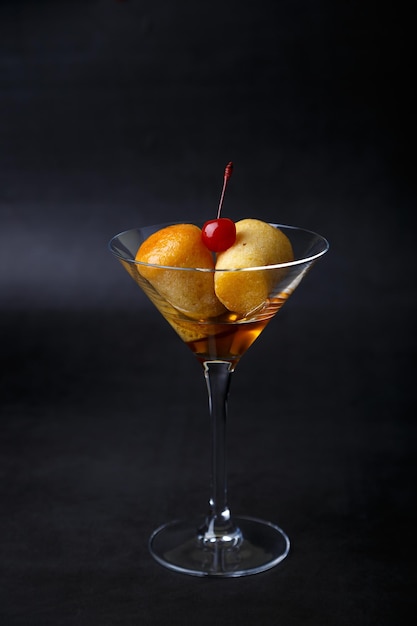 Neapolitan rum baba or baba au rum in a martini glass with a
cocktail cherry on a black background small yeast cakes soaked in
rum syrup traditional italian pastry closeup selective focus