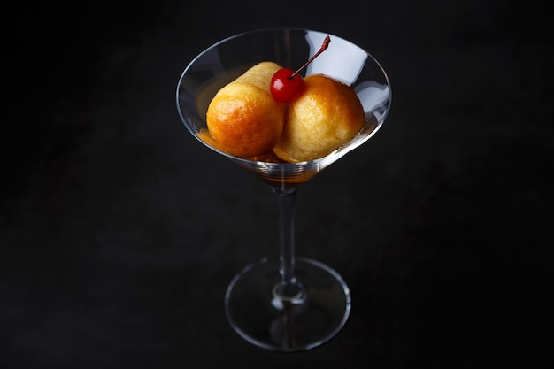 Neapolitan Rum baba or baba au rum in a martini glass with a cocktail cherry on a black background Small yeast cakes soaked in rum syrup Traditional Italian pastry Closeup selective focus