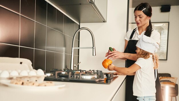 Photo near the sink mother with her daughter are preparing food on the kitchen