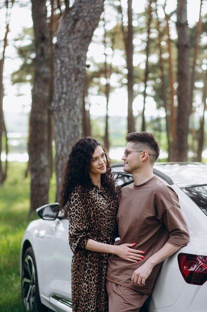 Near white colored car Beautiful young couple have a good time in the forest at daytime