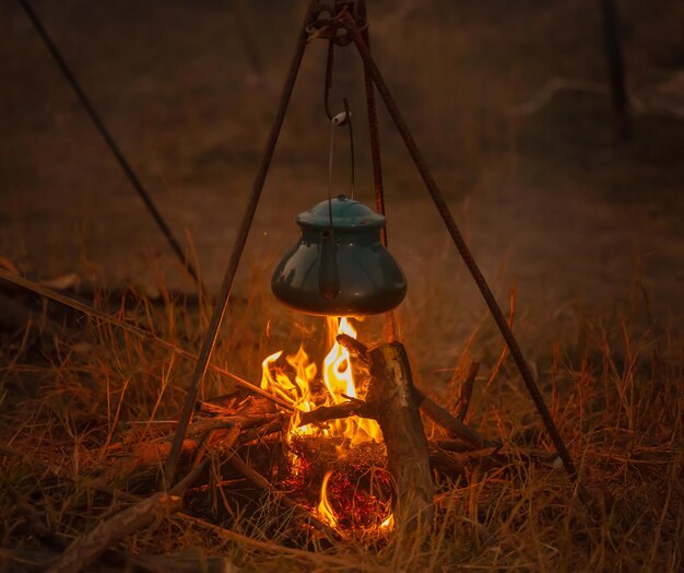 森の近くでキャンプの夜キャンプファイアの上で夕食を調理しています