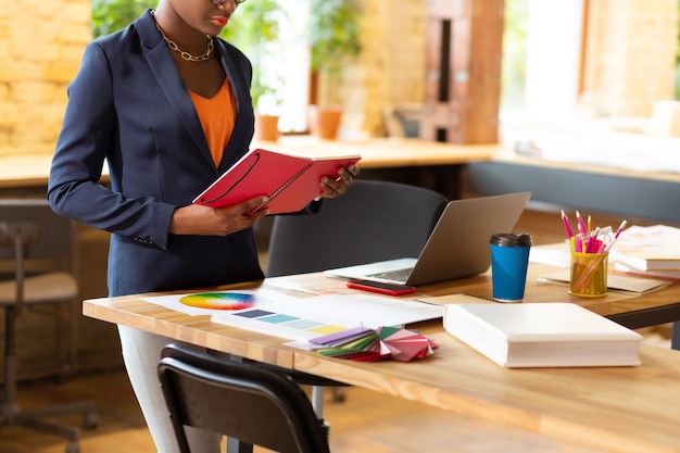 Near working table. Busy interior designer standing near her working table while working hard