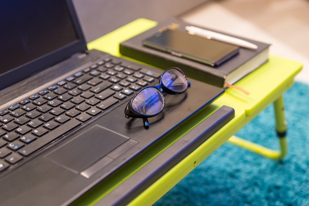 Neat tabletop workstation with eyeglasses lying on the keyboard of an open laptop computer with a diary and mobile phone alongside