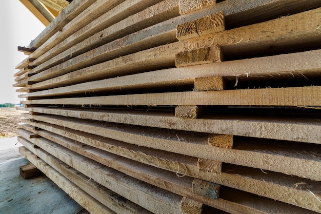 Neatly piled long stack of wooden boards inside attic room under construction.