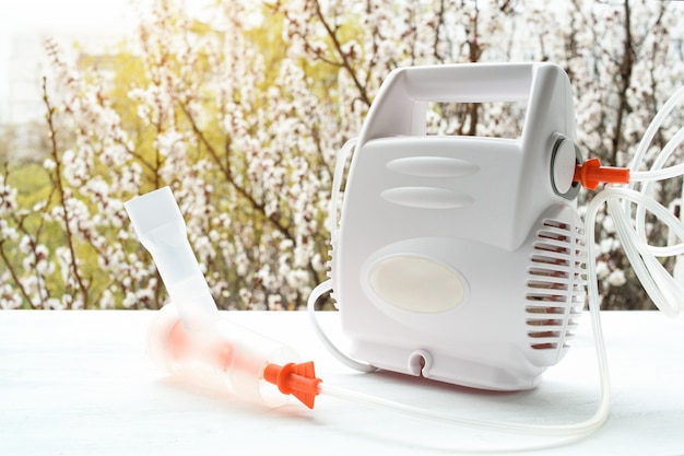 Nebulizer with a mask on the  of a blossoming tree. Spring exacerbation