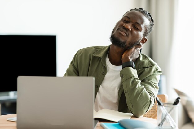 Neck ache Upset african american guy massaging aching neck suffering from pain after computer work sitting workplace