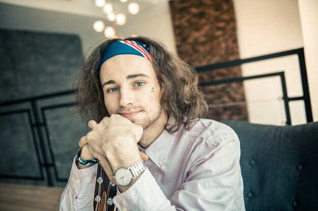 Neck of guitar. Smiling good-looking young artist with bright blue eyes putting chin on crossed hands