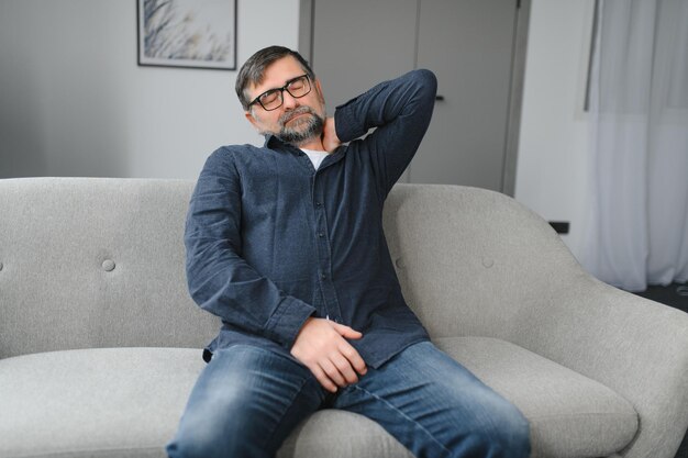 Neck Pain Portrait Of Exhausted Mature Man Massaging Aching Neck Suffering From Ache Sitting On Couch At Home In Living Room Osteoarthritis Older People Health Problem Sedentary Lifestyle Concept