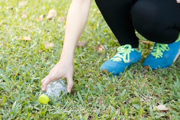 Nederig gedeelte van een vrouw die een plastic fles op het veld plukt