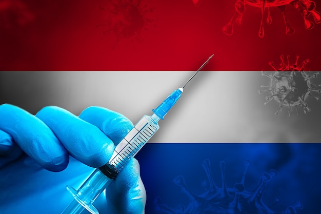 Nederland Covid19 Vaccinatiecampagne Hand in blauwe rubberen handschoen houdt spuit voor vlag