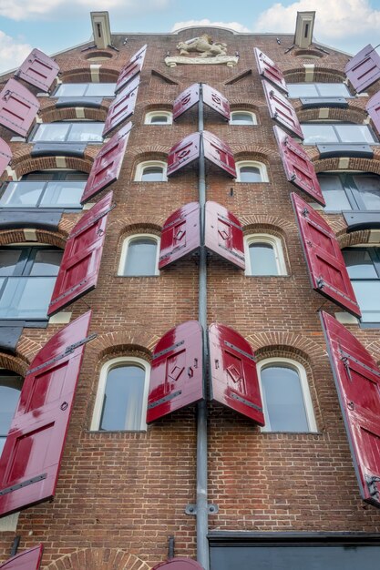 Nederland. een dagje amsterdam. onderaanzicht van een oud bakstenen huis met open rode luiken voor de ramen