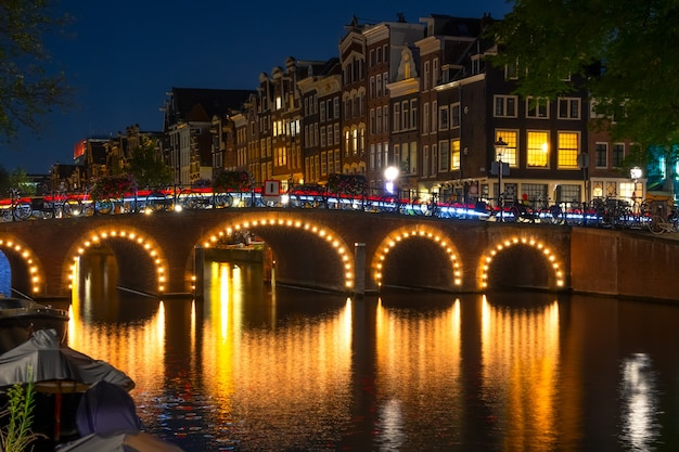 Nederland. Verlichte gracht bij nacht in Amsterdam. Veel fietsen staan bij het hek geparkeerd. Traditionele huizen met gloeiende ramen