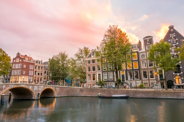 Nederland Zonsondergang op het Amsterdamse kanaal Oude stenen brug en typische huizen aan de kade Verkeer op het water en de straten