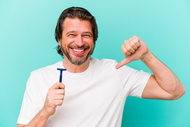 Nederlandse man van middelbare leeftijd met een scheermesje geïsoleerd op een blauwe muur voelt zich trots en zelfverzekerd, voorbeeld om te volgen