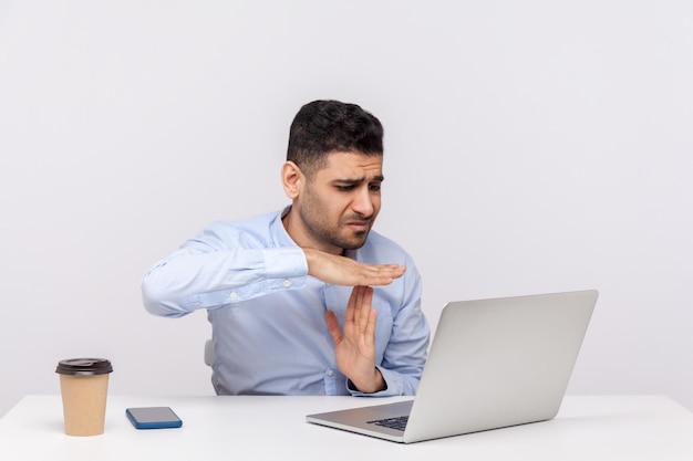 Need break. Upset male employee sitting office workplace, looking imploring at laptop screen and showing time out, asking pause in online conference. indoor studio shot isolated on white background