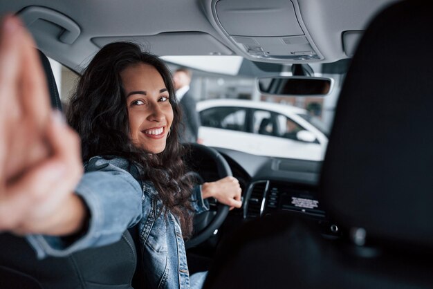 Foto devo catturare quel momento, una ragazza carina con i capelli neri che prova la sua nuova auto costosa nel salone automobilistico.