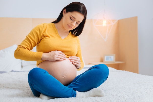 마사지가 필요합니다. 매력적인 미래의 엄마가 머리를 숙이고 아래쪽을 내려다 보면서 긴장을 풀고 하루를 보내고 있습니다.