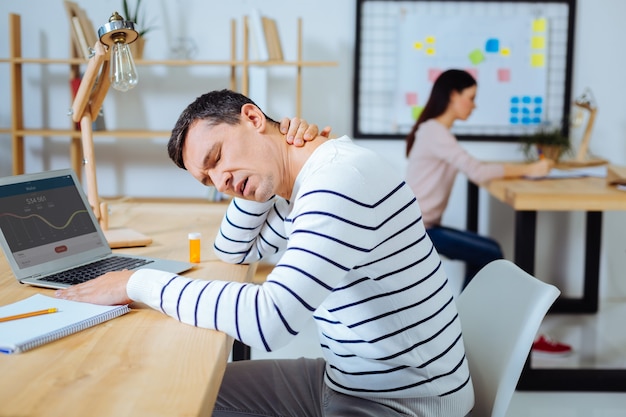 Need some rest. Tired male person opening mouth and putting arms on table while keeping eyes closed