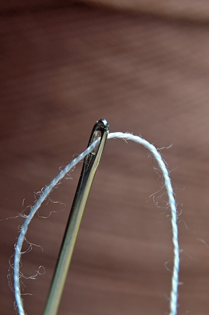 A needle with a thread inserted into it against the background of a large spool of thread. macro