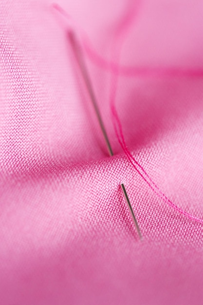 Photo needlework and tailoring concept - sewing needle with thread stuck into pink fabric