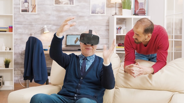 Foto neef leert zijn grootvader hoe hij een virtual reality-headset moet gebruiken in de woonkamer.